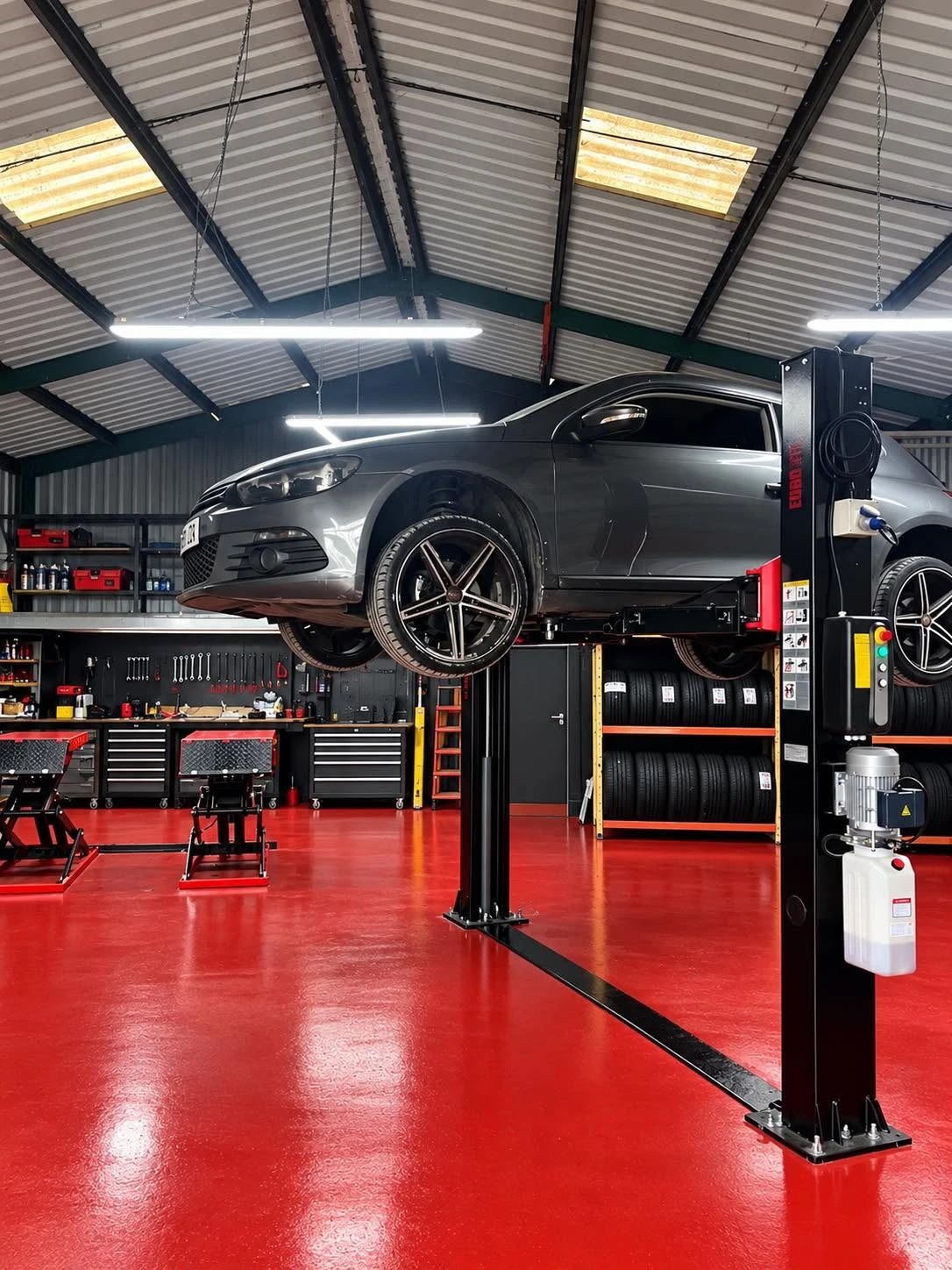 A car on the lift inside our Abergele workshop, with tyre racks behind